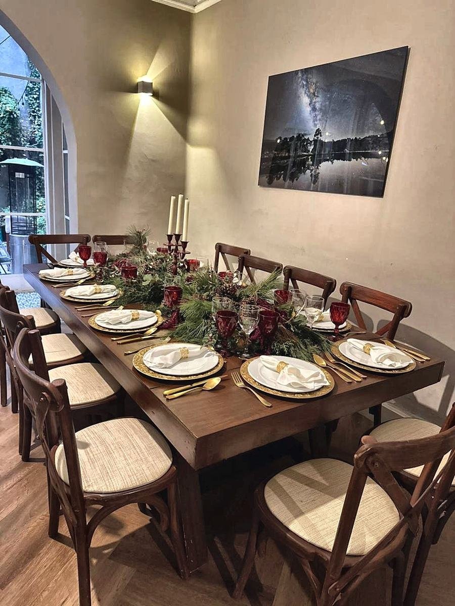 Mesa de cena de fin de año con platos base dorados, copas rojas y centro de mesa de pino
