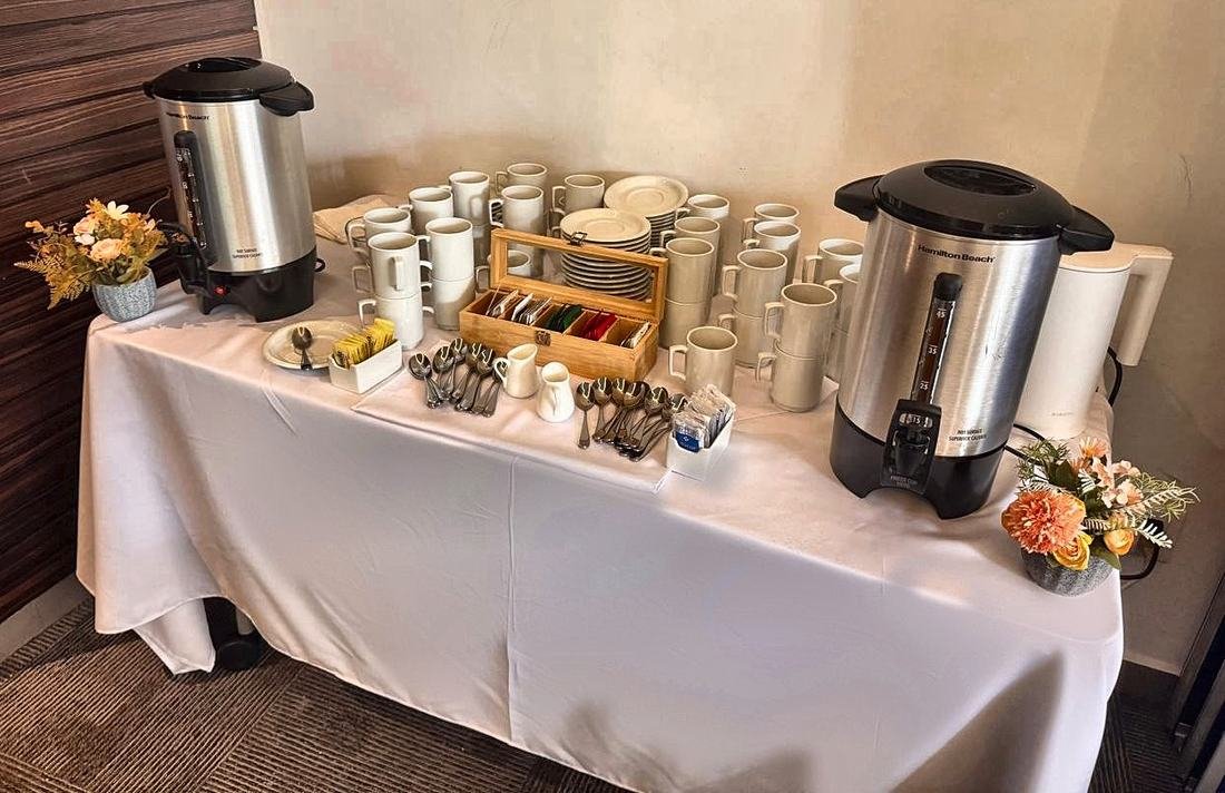 Estación de café con cafeteras, tazas blancas, caja de tés y cucharas